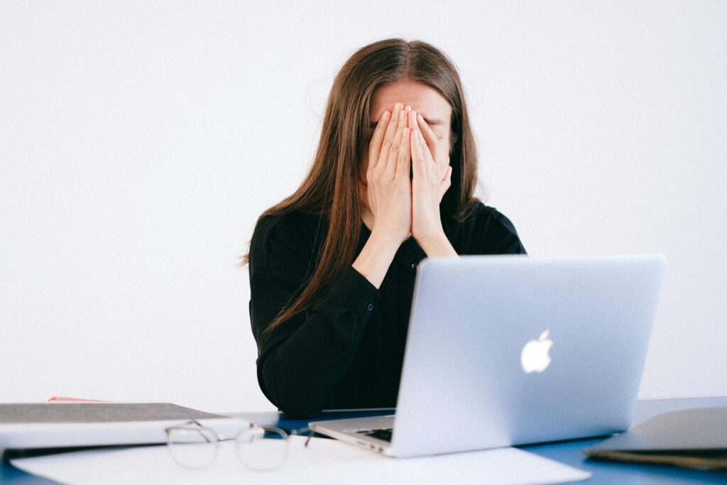 Fui demitido e não recebi todos os meus direitos: o que fazer? Woman feeling stressed and overwhelmed at her desk while working remotely on a laptop.